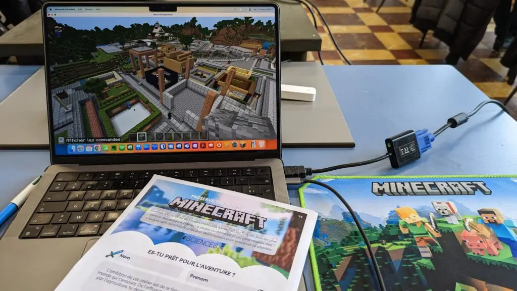 Ordinateur portable affichant un monde Minecraft Education, à côté d'une fiche d'activité eSCIENCES « Préserve ta planète avec Minecraft » et d'un tapis de souris Minecraft.
