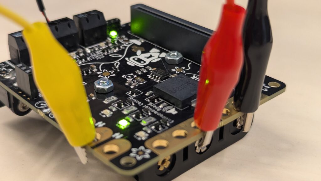 Carte électronique micro:bit reliée par des pinces crocodiles jaune, rouge et noire, avec ses voyants verts allumés