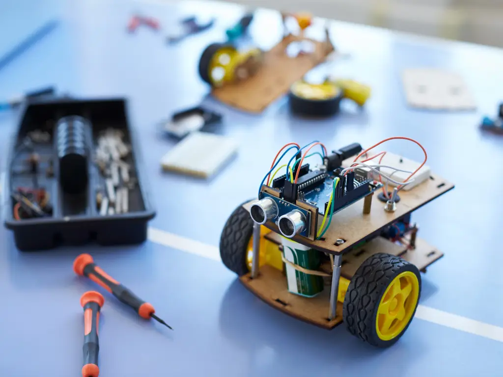 Petit robot roulant à carte Arduino, tournevis et pièces électroniques sur une table